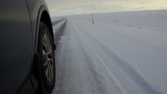 Close shot of a SUV tire driving on ice and snow over a frozen ground with sky in background