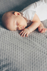 Sleeping baby boy in white bodysuit in bed with copyspace