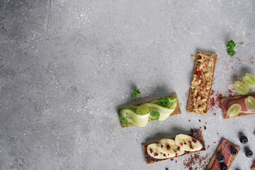 Healthy vegan sandwiches with hummus, guacamole, chocolate, cream, berries and raw spring vegetables on crispy rye bread. Flat lay on a gray background. Free empty space