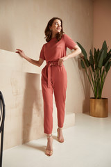 Beautiful woman fashion model brunette hair tanned skin wear pink red overalls suit sandals high heels accessory bag clothes style journey safari summer collection plant flowerpot wall stairs.