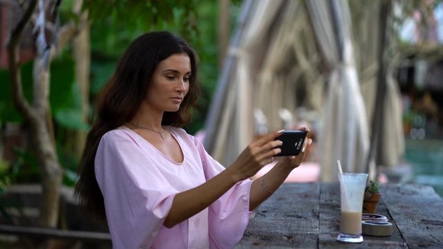 Young woman taking photo of cocktail with cellphone in park cafe