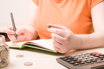 a woman holds a coin of 10 rubles and writes something in a notebook, copy space, coins on a table...