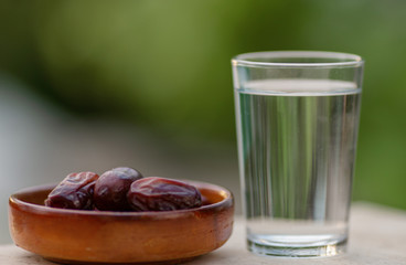 A glass of water and iftar dry dates on plate ready to eat for iftar time. Islamic religion and ramadan concept. Natural blured background with copy space.