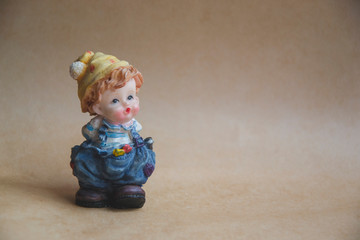 Small statue of boy in yellow hat and blue pants. Close up picture of home accessoire. Little boy on brown background. Greeting card. Wallpaper picture. Vintage doll.