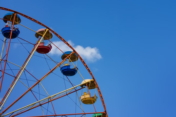 Fragment of a ferris wheel on a background of blue summer sky.