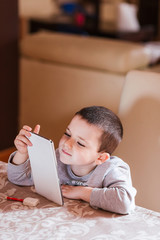 
little boy entertains himself watching content on a tablet pc sitting at home and smiling, relaxation concept