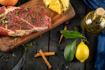 Raw meat on a wooden board with herbs and spices, served with cinnamon and lemon