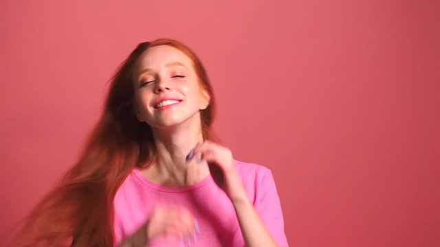 redhaired ginger woman in pink studio background ,her bun fell apart during shaking head