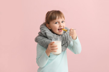 Little girl ill with flu holding glass of milk and eating honey on color background