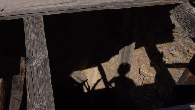 Mans shadow looking down into old verticle mine shaft.