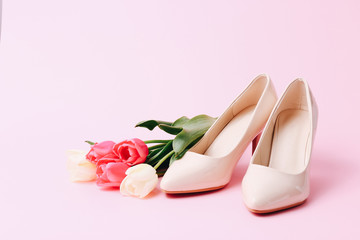 Fototapeta na wymiar Female high heel shoes with beautiful tulips on pink background