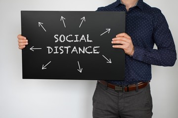 Man is holding black board with the chalk written text and logo Corona virus - Social distance.