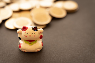 Maneki neko or beckoning cat, unfocused coins on the background. Conceptual symbol of luck, abundance and economic success.