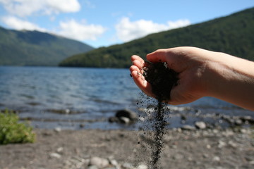 Small grains of black sand fall from a woman's hand, Lanín National Park, Argentina