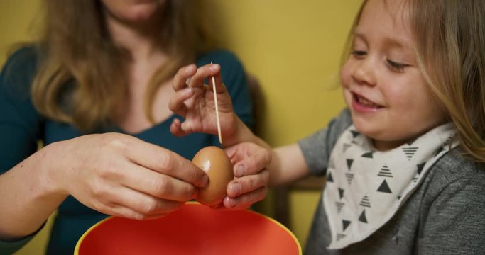 Mother helping preschooler pierce an egg for blowing out and decorating