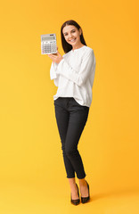 Young woman with calculator on color background - obrazy, fototapety, plakaty