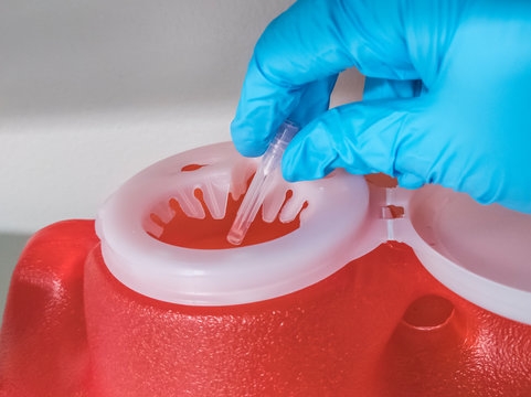 gloved hand dropping a used needle into a bright red sharps container