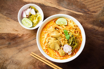 Traditional Northern Thai food (Khao Soi), spicy curry noodles soup with coconut milk and chicken in a bowl on wooden background, Top view