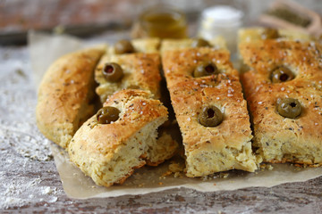 Selective focus. Macro. Fresh homemade focaccia with italian herbs. Cooking at home. Traditional italian bread with olives.