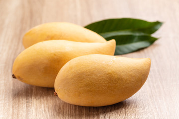 Ripe mango fruit with leaf on wooden background, tropical fruit, Thai mango (Nam Dok Mai)