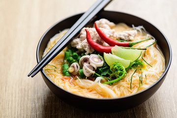 Spicy rice noodles soup with spices and herbs (Thai Tom Yum) in a bowl with chopsticks, Asian food