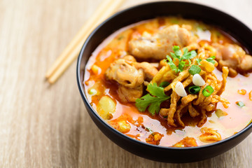 Northern Thai food (Khao Soi), spicy curry noodles soup with coconut milk and chicken in a bowl on wooden background	