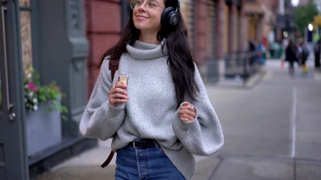 Carefree female tourist in spectacles dancing during city sightseeing feeling happiness during holidays for discover world, smiling hipster girl enjoying music and travel lifestyle
