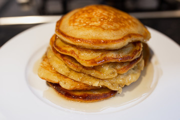 Fresh homemade classic pancakes with maple syrup in a white plate on a wooden board.