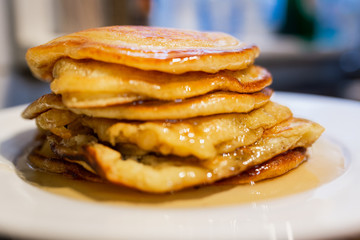 Fresh homemade classic pancakes with maple syrup in a white plate on a wooden board.