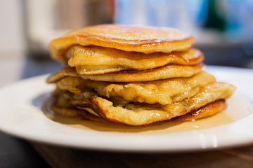 Fresh homemade classic pancakes with maple syrup in a white plate on a wooden board.