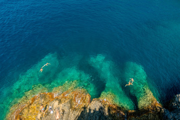 A cenital view of some people swimming in the sea with a rocky coastline.