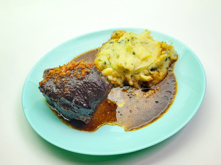 on a blue takeaway plate, a piece of beef with mashed potatoes on a white background.