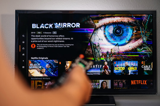 Paris, France - Jul 10, 2019: Senior Man Hand Holding Remote Control Watching The Black Mirror On Netflix - It Is A British Science Fiction Anthology Television Series Created By Charlie Brooker,