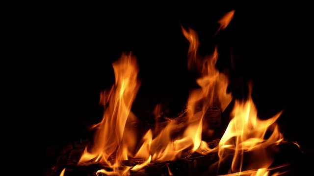 Hot fire and flickering flames from wood logs burning in a fireplace, with dark background and copy space on left, in a relaxing closup clip in a loop. Relaxation concept.