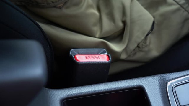 Hand of wonderful young Caucasian woman in winter green jacket press a red button, unfastening safety automobile seat belt in the car close up. Closeup of auto protective gear.  Driver safe concept.