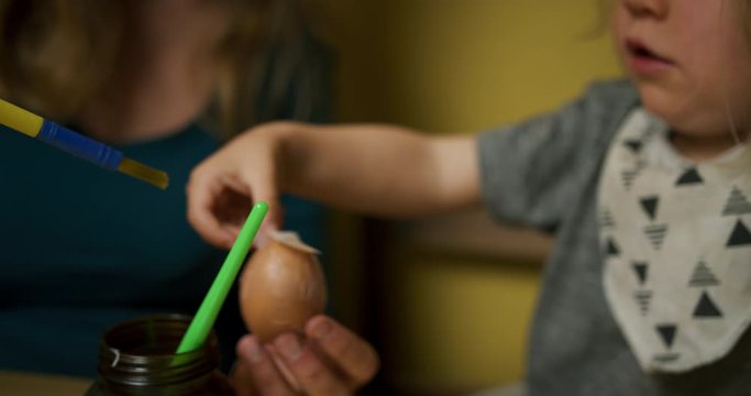 Mother showing preschooler how to decorate Easter eggs