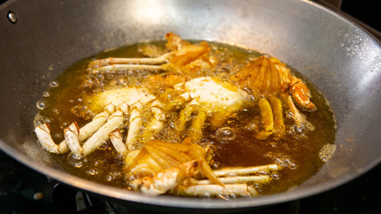 Close up view of crab being deep fried in a hot boiling oil in metal wok.