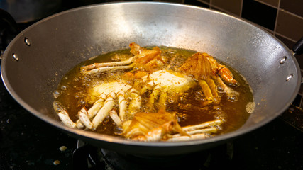 Close up view of crab being deep fried in a hot boiling oil in metal wok.