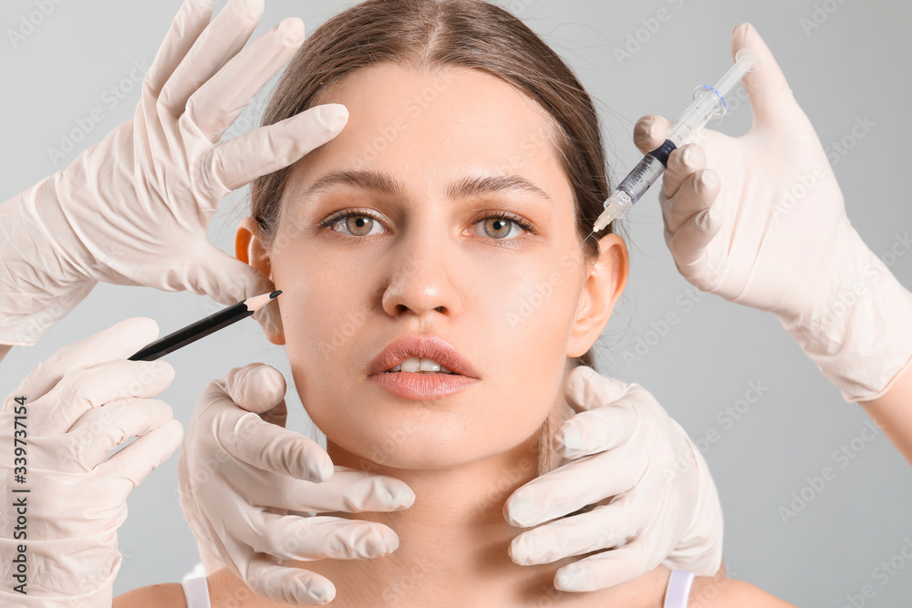 Sticker young woman and hands of plastic surgeons with pencil and syringe on grey background