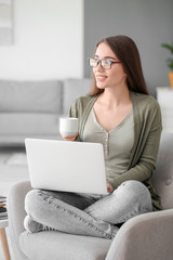 Beautiful young woman working on laptop and drinking coffee at home