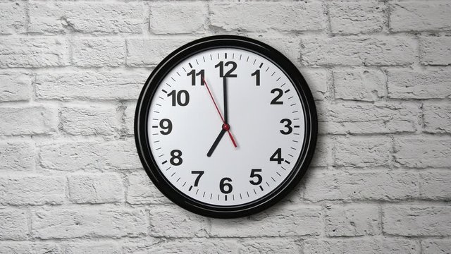 The Time Is 7.00 AM Or PM On A Black Wall Clock With A Red Second Hand On A White Brick Wall.