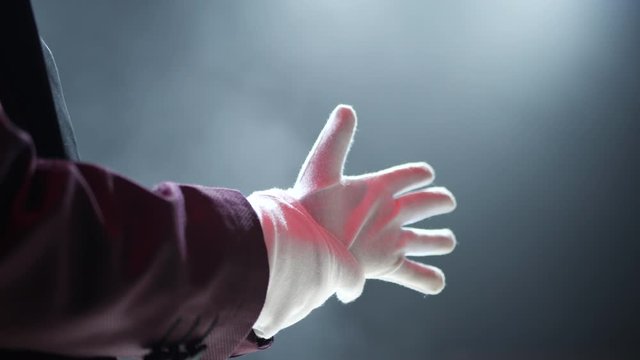 The magician wears gloves on the stage of the circus. Close-up.