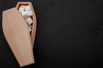 Fototapeta na wymiar Diabetes disease, insulin resistance and added sugars are killing you concept with coffin filled with sugar cubes isolated on dark black background with copy space
