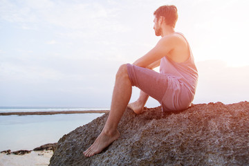 Fototapeta na wymiar Young man sitting on a rock above a beautiful coastline