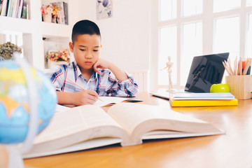 Young student boy makes his exercise sitting at table. Students studying and reading with books in library. Students doing his homework for elementary school. education and back to school concepts.