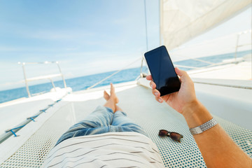 Phone in the hand of a vacationer on a yacht - Powered by Adobe