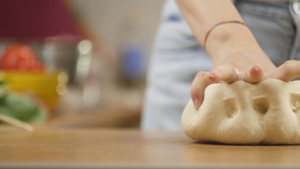 woman on the kitchen table makes domestic food pizza, hands work and pushing stir knead the dough, selective focus dolly shot