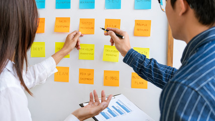 Business people arranging sticky notes commenting and brainstorming on work priorities colleague in...
