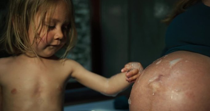Little boy having a bath and putting bubbles on his pregnant mother's belly
