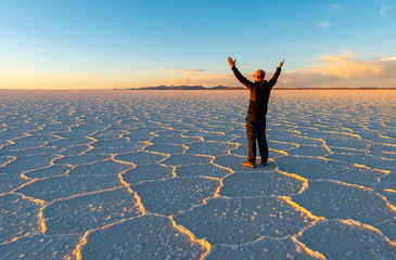 Sunset of the Uyuni Salt Flat Desert with Hexagon salt formations and a caucasian male tourist with...